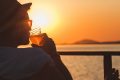 man sipping a beer while watching the sunset over the ocean